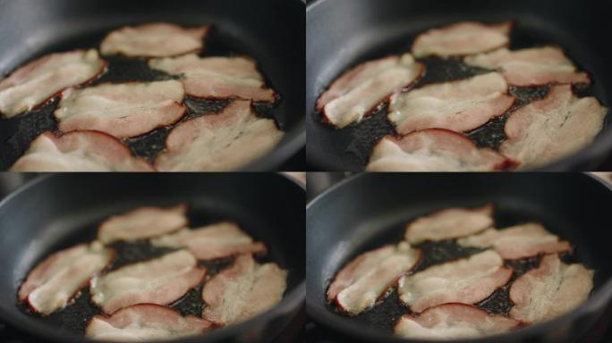 平底锅炸的脆皮培根片。烹饪有机培根切片的慢动作镜头。锅中的脂肪散落