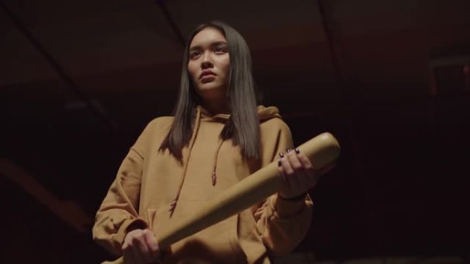 好斗的亚洲女罪犯拿着棒球棒站在黑暗的大楼里