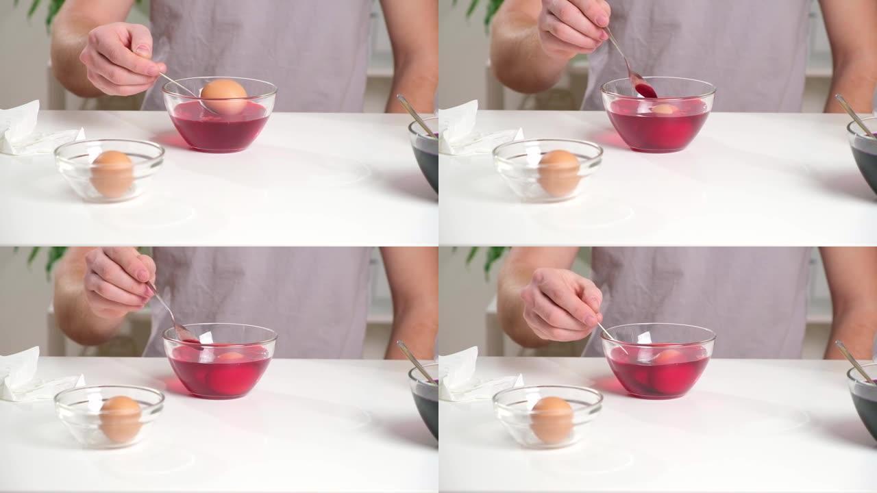 一个人将鸡蛋放在勺子上，放入装有染料的玻璃杯中。用复活节彩蛋染色鸡蛋