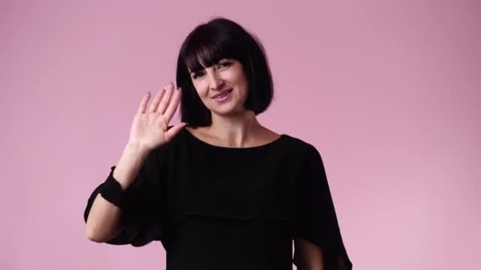 一个女人在粉红色背景上挥手打招呼的4k视频。