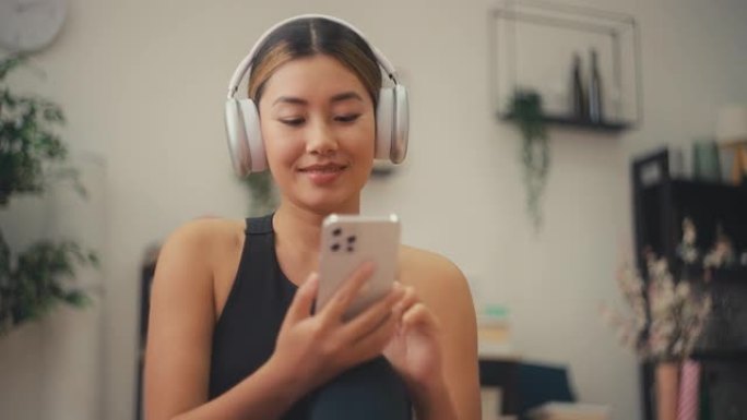 戴着耳机的韩国快乐女人在智能手机上选择歌曲进行家庭锻炼