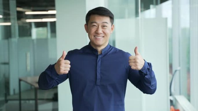 满意的亚洲商人肖像在现代办公中心表现出竖起大拇指的手势快乐积极
