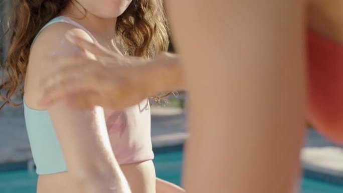 母亲在女儿皮肤上涂抹防晒乳液以保护阳光小女孩准备和妈妈一起在游泳池游泳，在阳光明媚的日子用防晒霜照顾