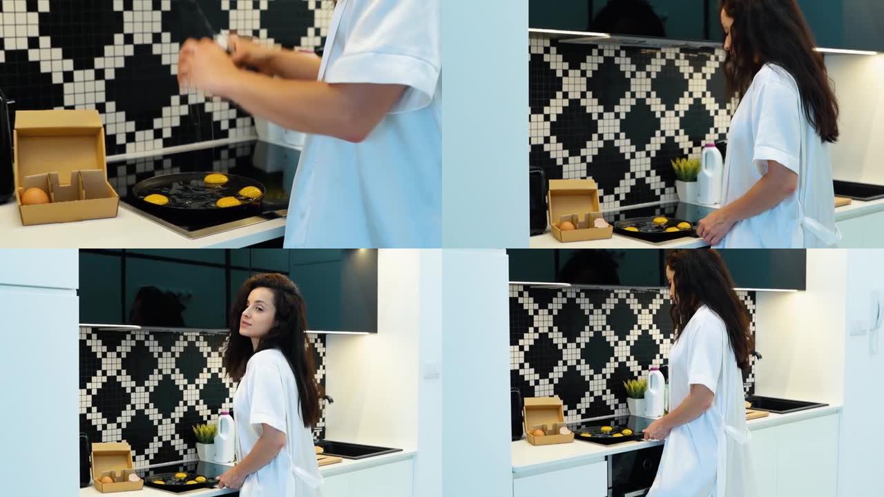 高加索人积极年轻迷人的女人在家煮鸡蛋。穿着内衣和白袍的性感美女在厨房准备早餐。食物准备。实时