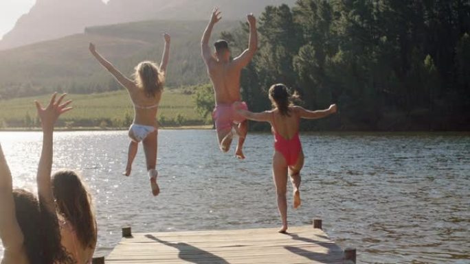 慢动作朋友在日落时从湖边的码头上跳下来，在水中嬉戏享受自由分享假期中的夏季冒险