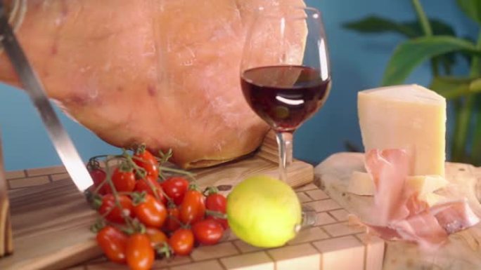 皇家jamon腿放在蓝色背景的木制架子上，腌制的火腿切片落在帕尔马干酪，柠檬，一杯红酒和西红柿附近的
