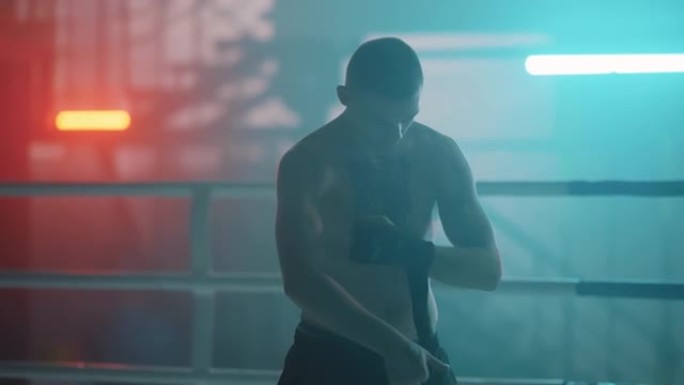 纹身的高加索运动员拳击手在带有bokeh灯的盒子上系上带子