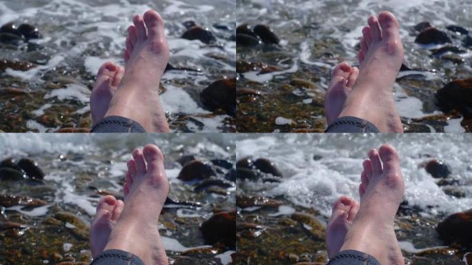 一个女孩的腿被波浪淹没的特写镜头。鹅卵石海滩女性腿上嘈杂的海浪