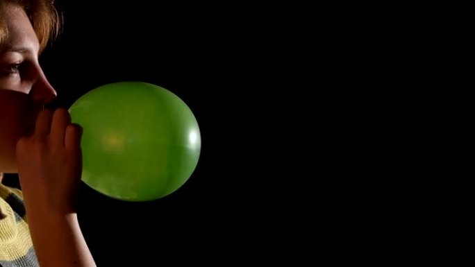 女孩吹绿色气球孤立在黑色背景，慢动作