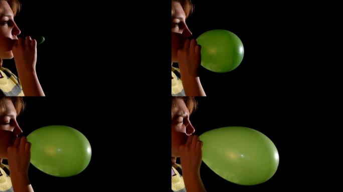女孩吹绿色气球孤立在黑色背景，慢动作