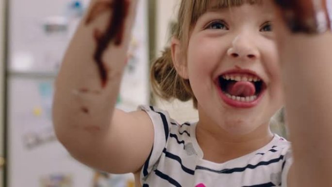快乐的小女孩，双手覆盖着巧克力舔手指，在厨房里玩得开心，顽皮的孩子玩耍，享受童年