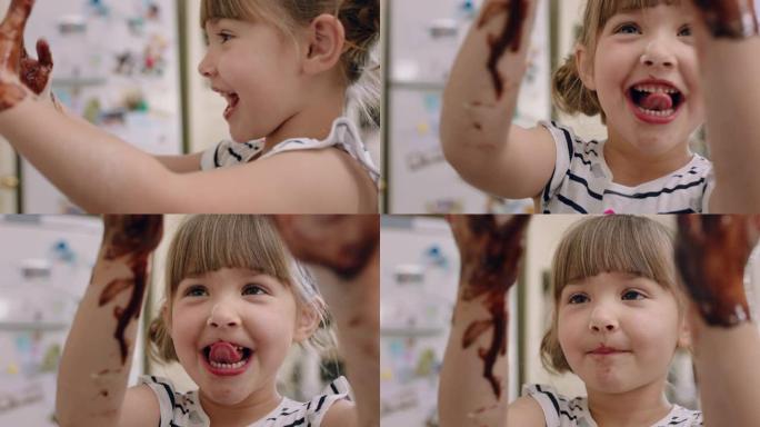 快乐的小女孩，双手覆盖着巧克力舔手指，在厨房里玩得开心，顽皮的孩子玩耍，享受童年