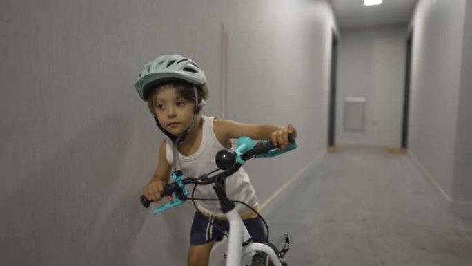 孩子在公寓走廊上骑自行车外出。一个戴着头盔的小男孩。孩子按下电梯按钮准备自己走