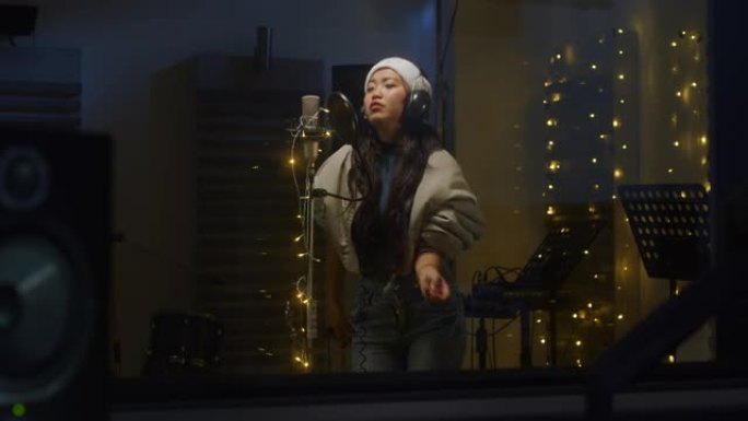 一位专业的亚洲女歌手在录音室为她的圣诞节专辑录制歌曲的肖像。美丽的年轻艺术家，戴着圣诞老人的帽子，喜