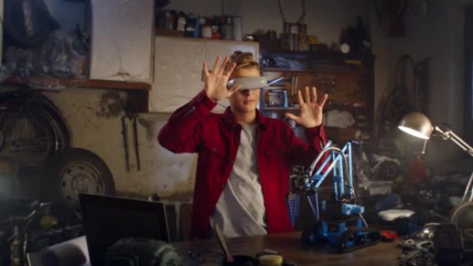 一个好奇的十几岁男孩的肖像，他戴着VR眼镜，在他父亲的工作室里为学校的创新工程项目测试机械臂。聪明的