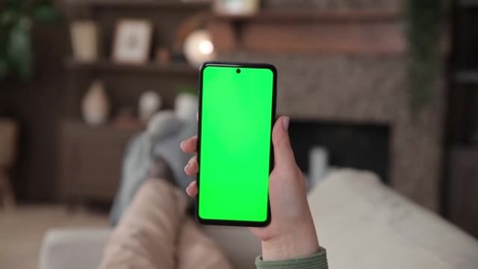 女人躺在沙发上的观点使用色度键绿色屏幕的智能手机。用于广告应用程序或流媒体服务的Chromakey模