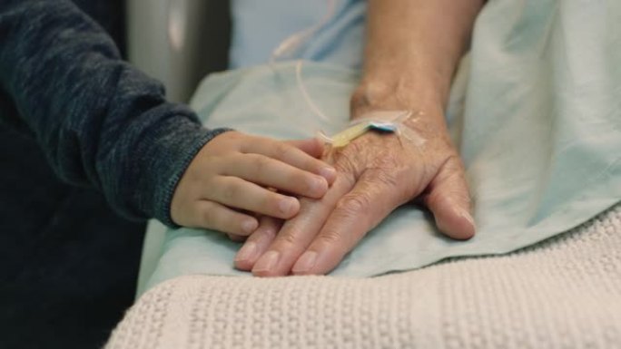 小男孩触摸祖母的手躺在医院的病床上，孩子在床边对奶奶从疾病中康复表示爱意。