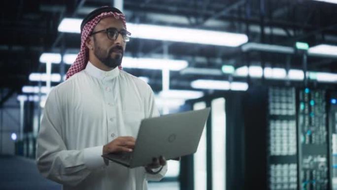 沙特系统管理员在数据中心的操作服务器机架行之间行走。工程师在网络安全和数据保护设施中使用笔记本电脑进