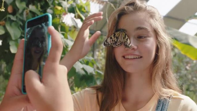 女孩脸上美丽的蝴蝶与快乐的朋友用智能手机拍照朋友在动物园野生动物保护区玩得开心在社交媒体上分享自然游