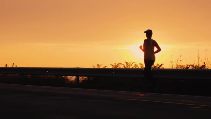 日落时，一名年轻活跃女子在海边的一条路上慢跑的剪影