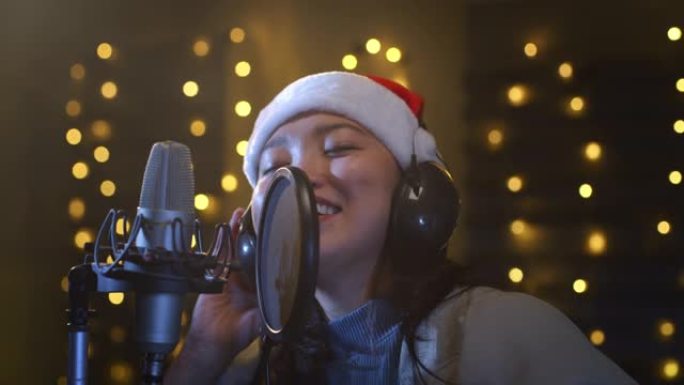 专业亚洲女歌手的特写肖像在录音室为她的圣诞节专辑录制了一首歌。热情洋溢的年轻艺术家，戴着圣诞老人的帽