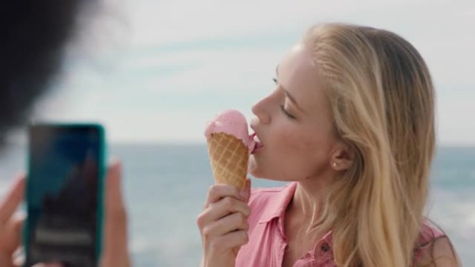 美丽的金发女人，非洲在海滩上吃冰淇淋，为朋友拍照，使用智能手机女孩朋友在社交媒体上分享快乐的夏日4k