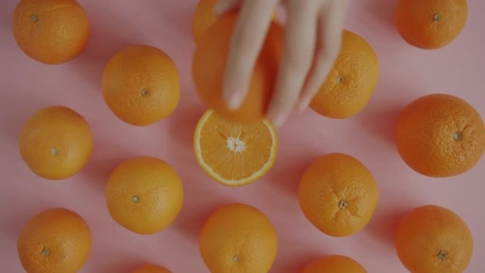 女性手从粉色桌子上拿新鲜有机橙的俯视图