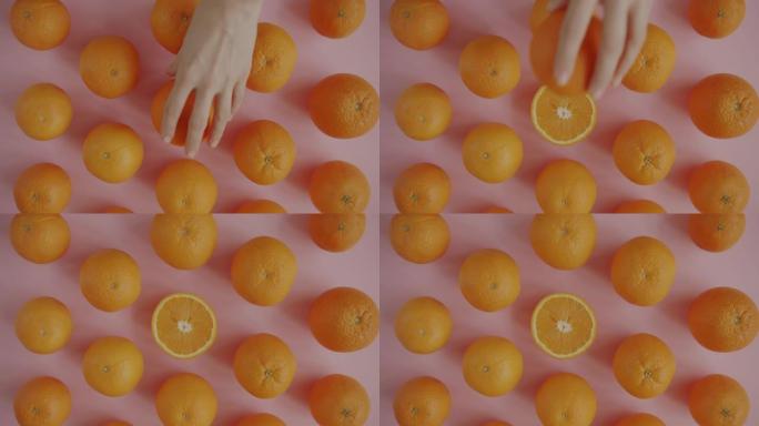女性手从粉色桌子上拿新鲜有机橙的俯视图
