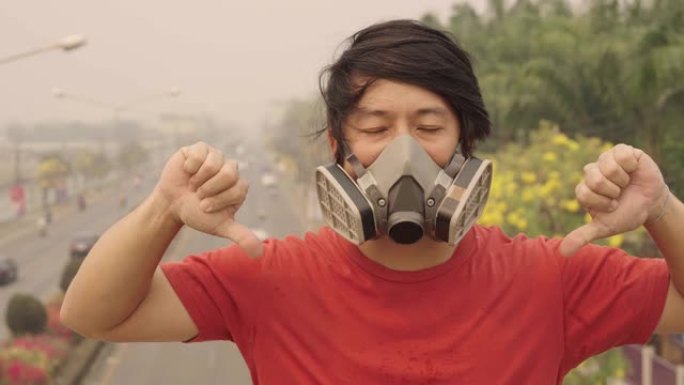 戴着污染面具的亚洲男子失望的拇指向下在下午2.5空气污染在天空户外