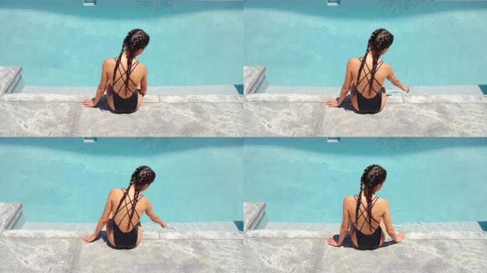 旅行女子坐在游泳池边嬉戏地抚摸着水面，在豪华酒店度假村享受美丽的海景，棕榈树穿着性感比基尼4k