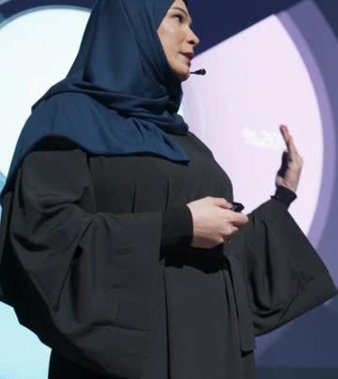 垂直屏幕: 成功的中东女性演讲者展示了新产品，在大屏幕上显示了信息图表，统计动画。在新闻发布会上谈论