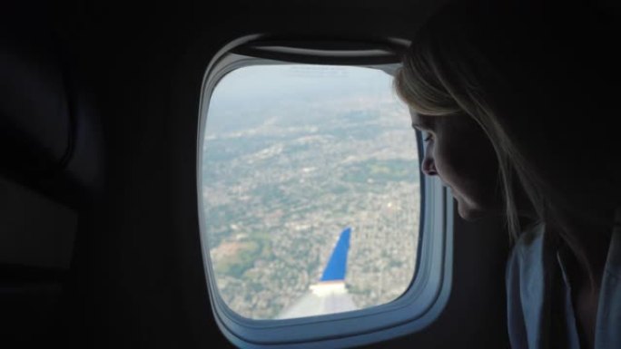一名年轻的女乘客从飞机的窗户望向远处的地面，那里可见大都市