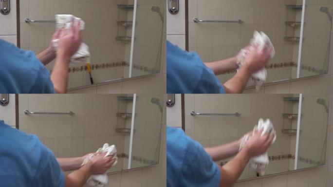 男人在浴室里用抹布擦拭镜子。