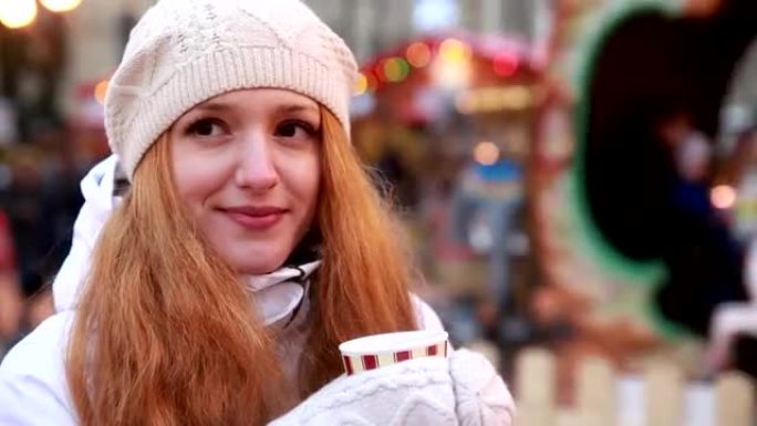 年轻迷人的女人在圣诞集市上喝热茶。