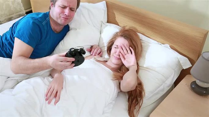 这对夫妇不想一大早起床。男人把闹钟藏在枕头下。