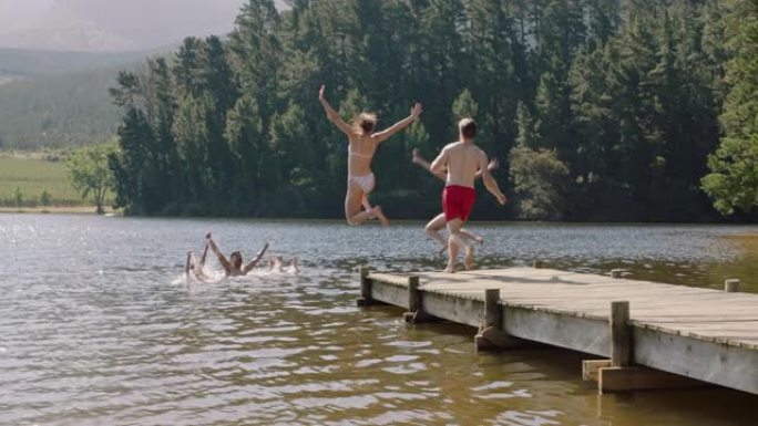 快乐的朋友在湖中跳下码头，在水中嬉水享受自由，在假期享受快乐的夏季冒险