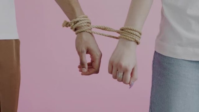 双手的特写男性和女性用绳子绑着移动试图在粉色背景上分离