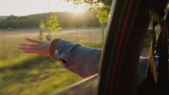 女人在车里牵着手走出窗户感觉风吹过手指在乡下开车暑假旅行享受日落路上的自由