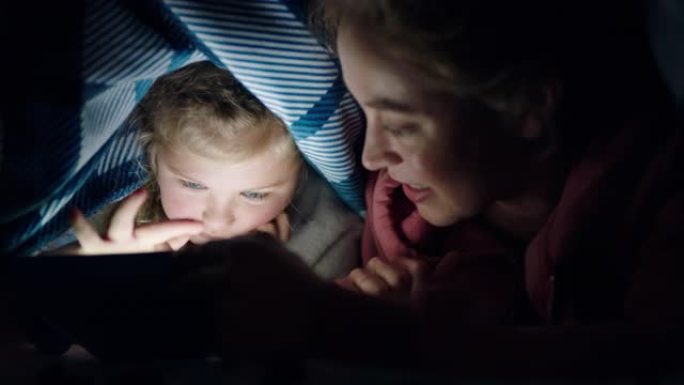 快乐的母女俩在毯子下使用平板电脑在触摸屏技术上玩游戏睡前放松娱乐
