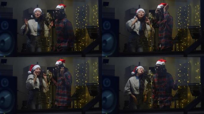 录音棚里两位多民族职业歌手的肖像，戴着圣诞老人的帽子，一起热情地唱歌。年轻的黑人和亚洲妇女在圣诞节的
