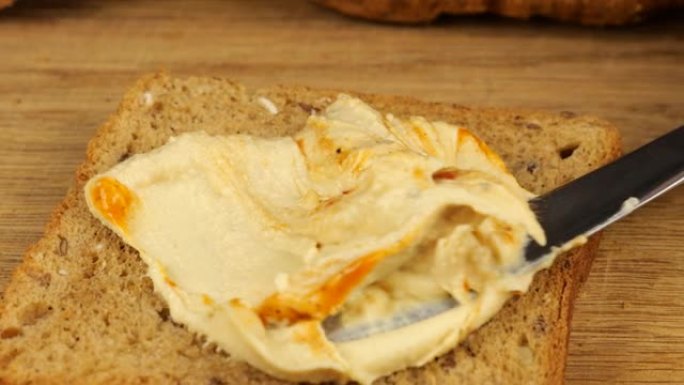鹰嘴豆泥用刀子铺在一块木菜板上的杂粮面包上。素食主义者的食物。
