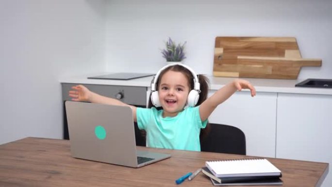 微笑的小女孩在在线课程结束时举起双手并感到高兴。