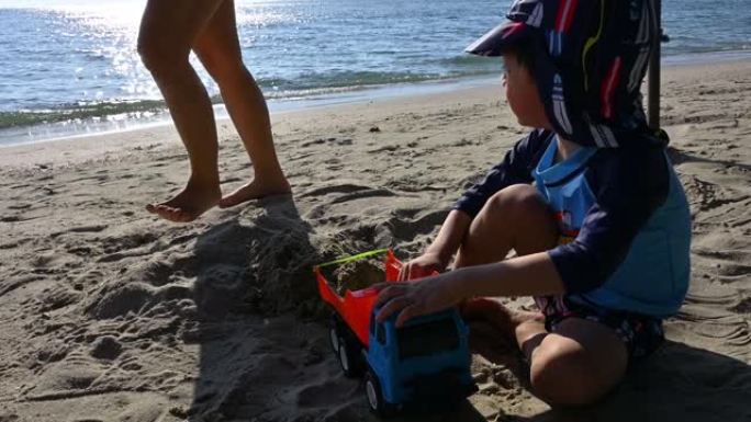 手持镜头，玩玩具自卸车的快乐孩子在假期的沙滩上玩得开心