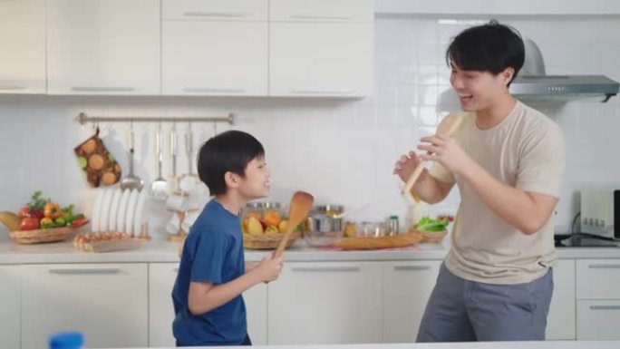 亚洲父子一边做饭，一边在家里的厨房里快乐地跳舞。单身父亲概念