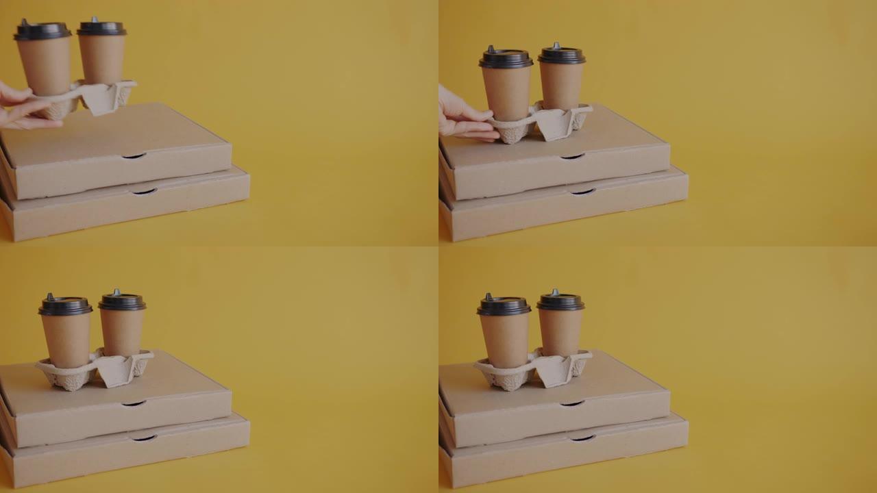 女性手的特写把咖啡杯带披萨的纸板箱放在黄色背景上