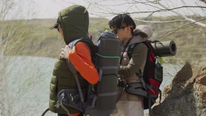 在岩石海岸上的两名亚洲女性游客，其中一名帮助其他人将背囊
