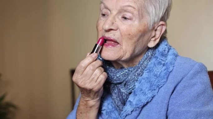 白发蓝眼睛的老年妇女用口红涂嘴唇。化妆和衰老概念。老年人的健康和福祉。手握红色唇彩