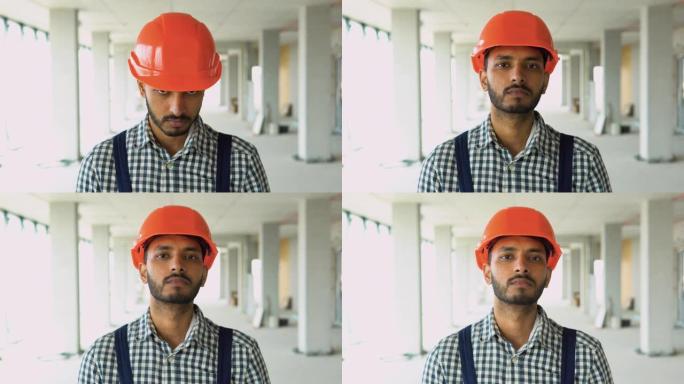 穿着制服的印度工人建筑工人的肖像戴着安全帽看着相机，站在办公中心的建筑工地上