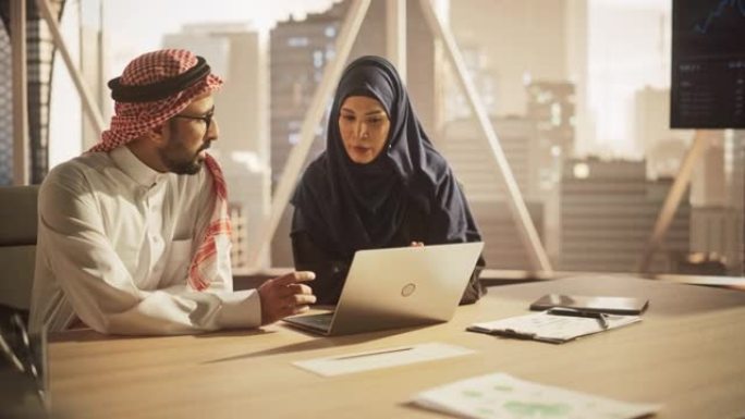 阿拉伯金融分析师开会与一位女性团队负责人讨论一个项目。中东同事使用笔记本电脑，在现代办公室工作，戴着