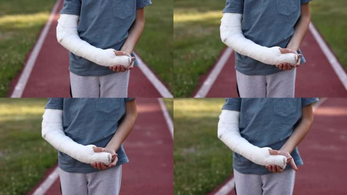 夏日在运动场上户外断手小男孩的剪辑视频。9岁肢体骨折的孩子。手臂上的石膏。健康和医学概念